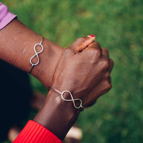 two women hold hands wearing infinity bracelet